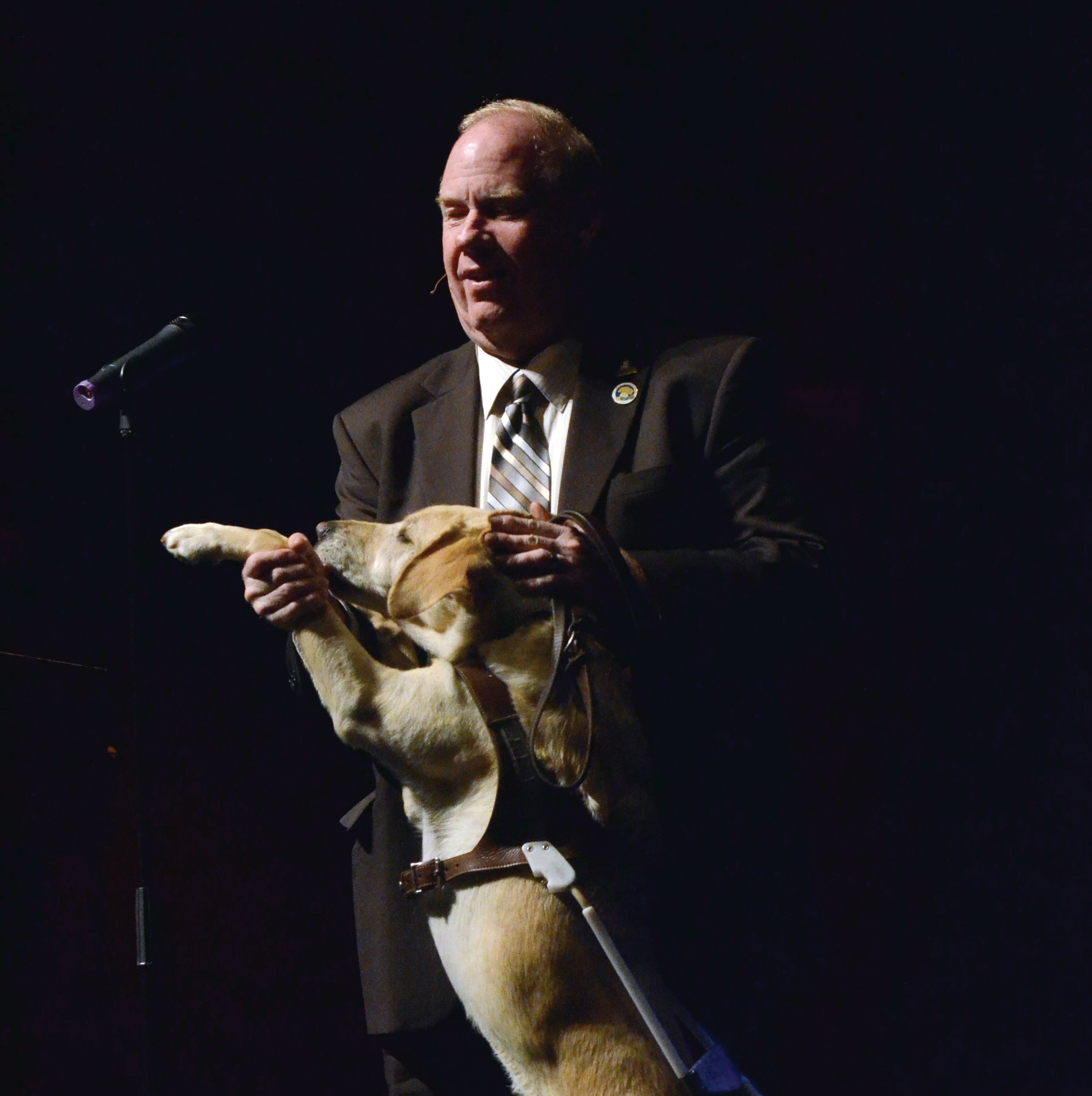Michael Hingson at a podium with his guide dog Africa.